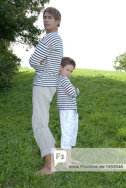 Vater und Sohn (4-7) im Park stehend  Rücken an Rücken