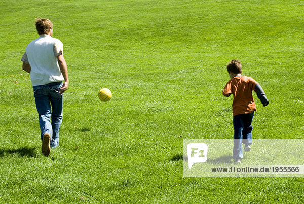 Vater und Sohn (4-7) spielen Fußball im Park  Rückansicht