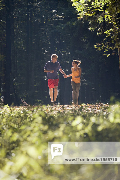 Junges Paar beim Joggen im Wald  Händchen haltend