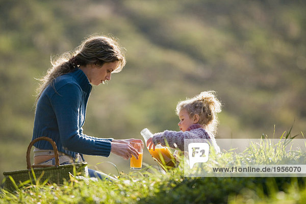 Mother sitting with daughter in meadow  mother pouring juice