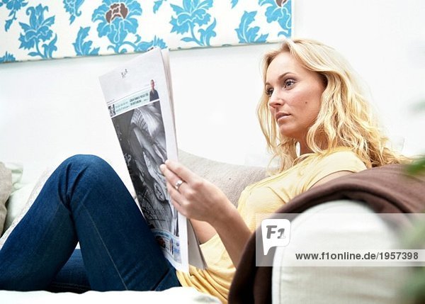 Junge Frau sitzt in einer Couch und liest Zeitung.