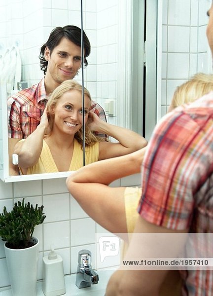Junges Paar schaut sich im Badezimmerspiegel an.