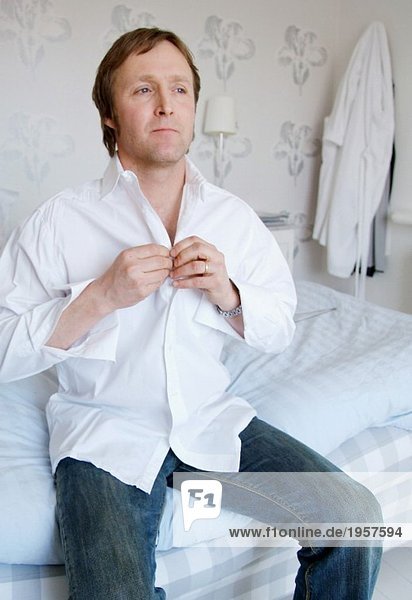 Mann auf der Bettkante sitzend und Knopfhemd