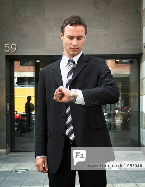Junger Mann im Anzug mit Blick auf seine Uhr