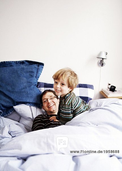 Junge spielt mit einem Elternteil im Bett