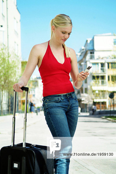 Junge Frau mit Koffer sendet SMS