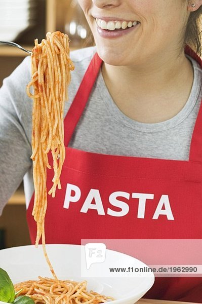 Junge Frau mit Schürze isst Spaghetti mit Tomatensauce