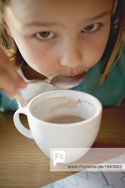Kleines Mädchen löffelt Kakao aus der Tasse