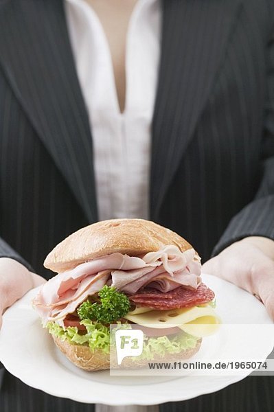 Woman holding a ham and cheese sandwich on a plate