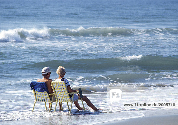 Seniorenpaar  sitzen mit Klappstühlen am Strand am Wasser
