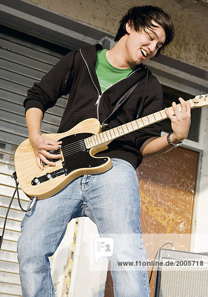 Junger Mann  asiatisch  spielt vor Lagerhalle E-Gitarre