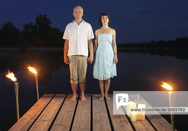 Paar  stehen abends nebeneinander auf Steg an See