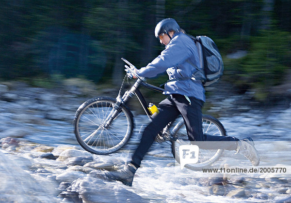 Mann springt mit Mountainbike über Bergbach  Bewegung
