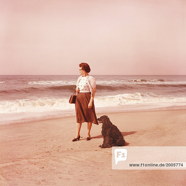 Nostalgiefoto  Frau mit Hund steht an Sandstrand