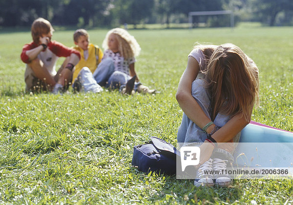 Teenager-Mädchen sitzt traurig allein auf Wiese