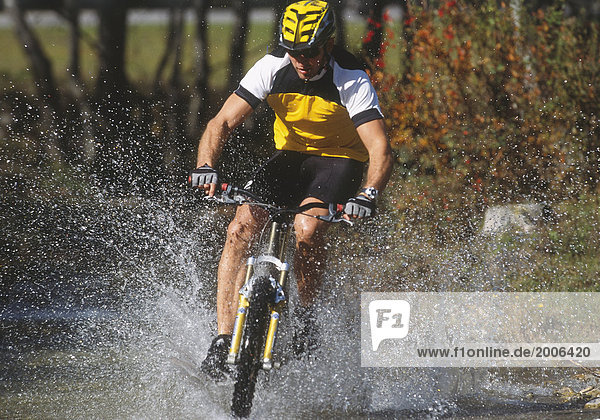 Mountainbiker fährt durch Bach  spritzendes Wasser