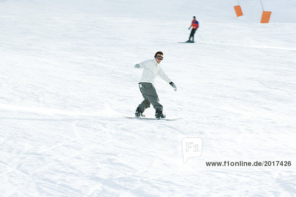 Young man snowboarding on ski slope  full length  skier in background
