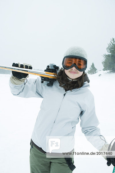 Teenage girl carrying skis on shoulder  smiling at camera