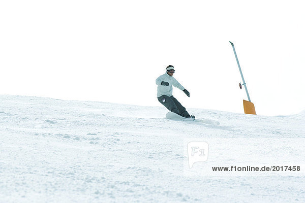 Young man snowboarding down ski slope  full length