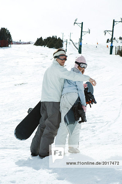 Two young snowboarders walking together  looking over shoulders at camera