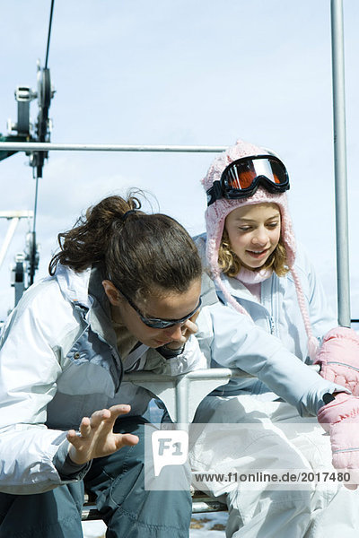 Two teenage girls sitting on chair lift together  looking over side