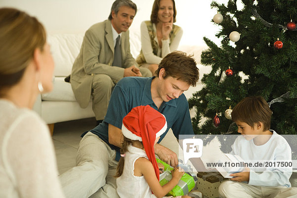 Vater und zwei Kinder am Weihnachtsbaum sitzend  gemeinsam Geschenke öffnen  Familie zuschauen