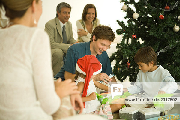 Vater und zwei Kinder am Weihnachtsbaum sitzend  gemeinsam Geschenke öffnen  Familie zuschauen