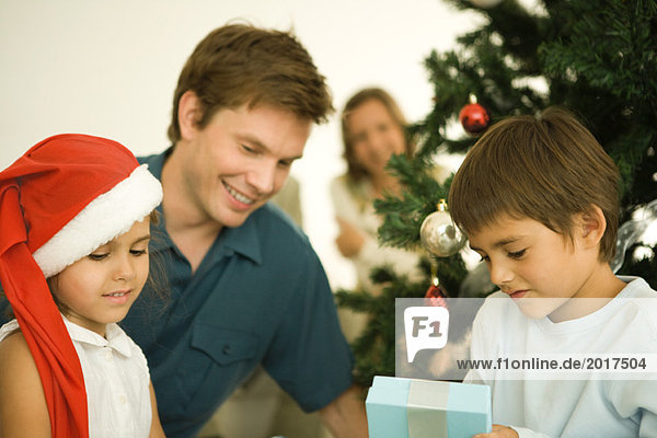 Vater und zwei Kinder am Weihnachtsbaum sitzend  Tochter mit Weihnachtsmütze  Sohn Eröffnungsgeschenk