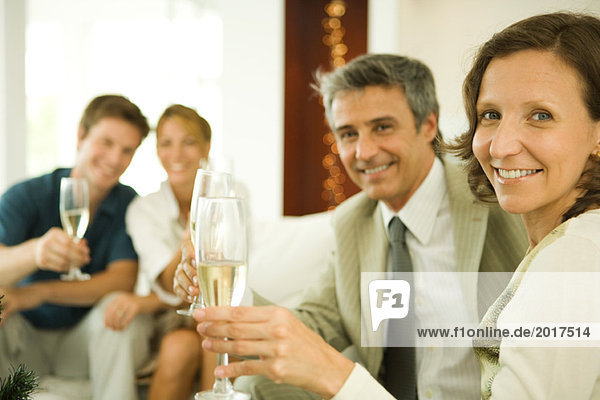 Paar macht einen Toast mit Champagner  lächelt in die Kamera  Freunde im Hintergrund