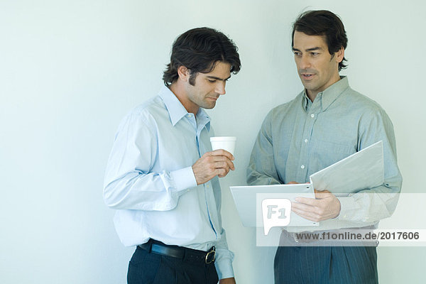 Two male colleagues looking at file together  one holding cup