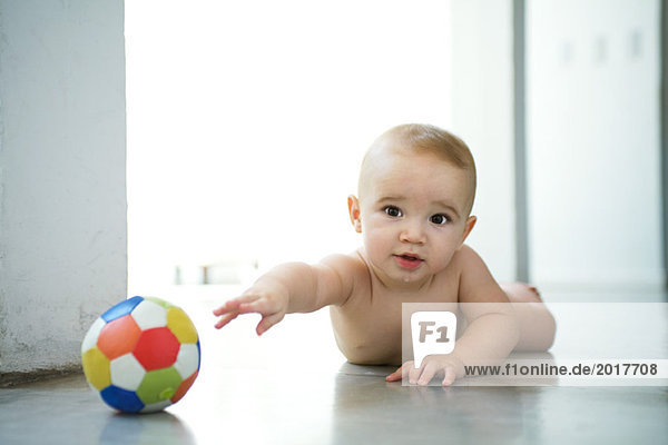 Baby lying on floor  reaching for ball and looking at camera