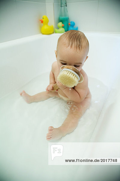 Babybadewanne  Badebürste gegen das Gesicht haltend  volle Länge