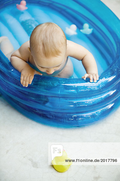 Baby im aufblasbaren Babybecken mit Blick auf die Gummidämmerung am Boden