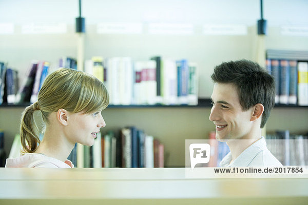 Studentinnen und Studenten lächeln sich in der Bibliothek an.