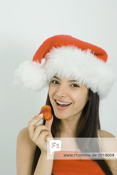 Junge Frau mit Weihnachtsmütze  Erdbeere hochhaltend  Kamera lächelnd  Portrait