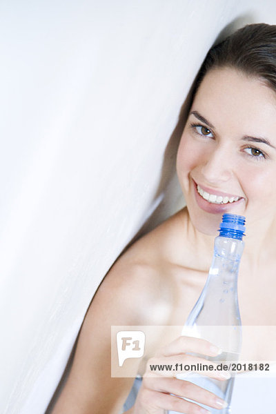 Junge Frau lehnt sich an die Wand  hält die Wasserflasche  lächelt die Kamera an.