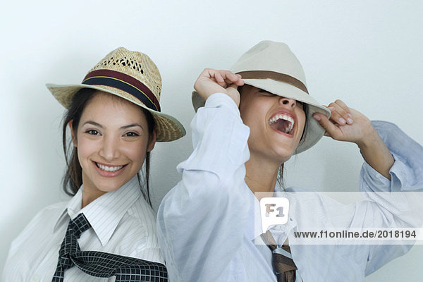 Two young female friends dressed in button down shirts  ties and hats  laughing  portrait