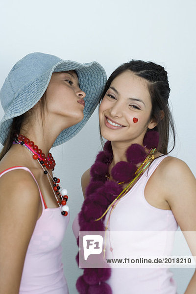 Two young female friends  one about to kiss the other's cheek  portrait