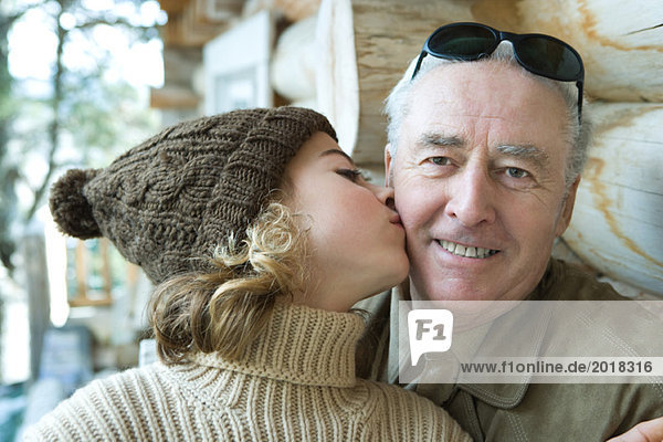 Älterer Mann lächelt in die Kamera  Enkelin küsst ihn auf die Wange  Porträt