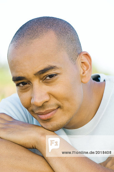 Man with shaved head smiling at camera  head resting on arms  portrait