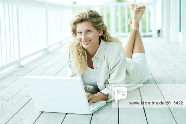Frau auf der Veranda liegend, mit Laptop, Kamera lächelnd, Portrait