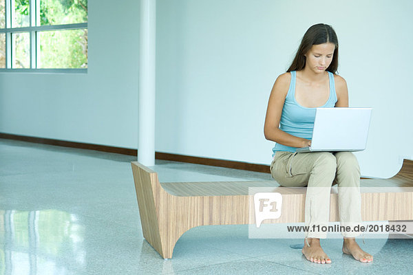 Teenage girl sitting on bench  using laptop computer  looking down