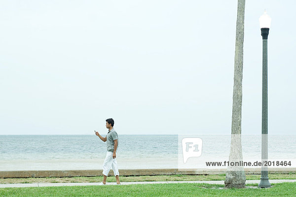 Mann  der auf dem Bürgersteig am Strand läuft und auf das Handy schaut.