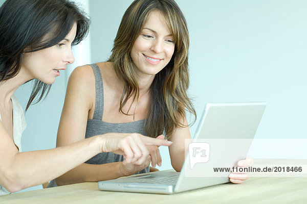 Two women sitting side by side  looking at laptop computer  one pointing
