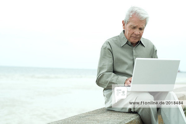 Älterer Mann  der draußen sitzt  den Laptop benutzt und nach unten schaut.