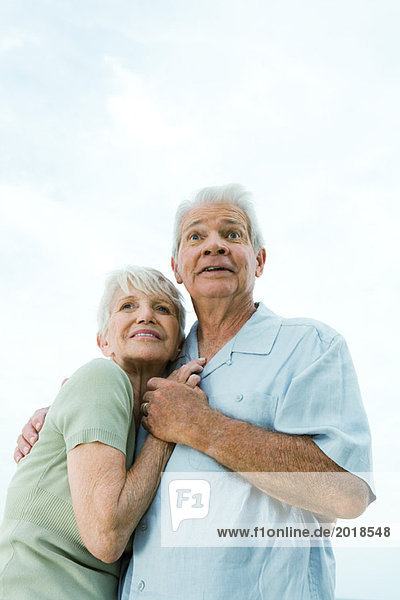 Seniorenpaar umarmt und schaut weg  Mann hebt die Augenbrauen  tiefer Blickwinkel  Taille nach oben