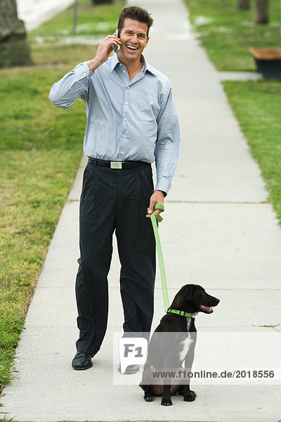 Mann geht Hund auf dem Bürgersteig  mit dem Handy