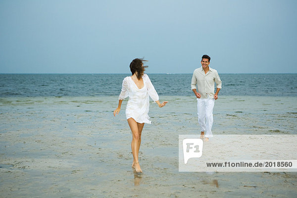 Mann und junge Begleiterin am Strand  auf Kamera zugehen  Mann im Hintergrund  volle Länge