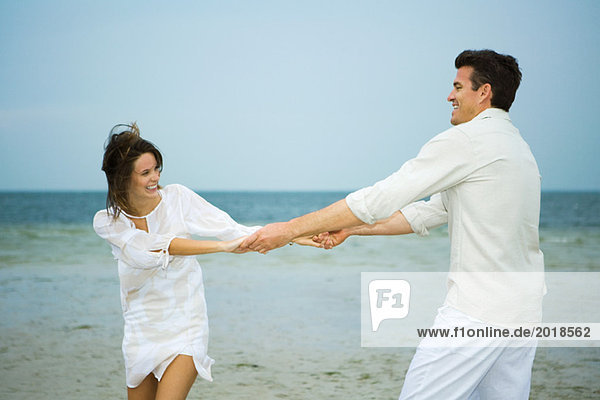Man and young female companion on beach  holding hands  swinging each other around
