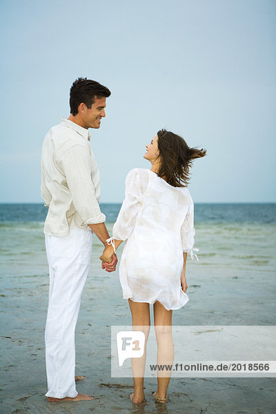 Mann und junge Begleiterin am Strand  Händchen haltend  einander anschauend  volle Länge